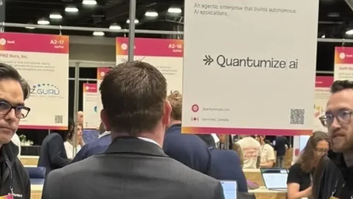 David Legendre, left, glasses and black quarter-zip, in conversation with a visitor at the Quantumize AI booth (SaaS, A2-01 ALPHA) during the Web Summit Vancouver 2026 Startup Showcase. A colleague stands at the right of the booth counter.